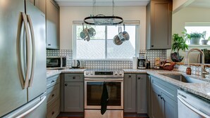 Een moderne keuken met roestvrijstalen apparatuur, een groot raam en een hangende kruidenrek.