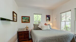 Een slaapkamer met een bed, nachtkastje, dressoir en kunstwerken aan de muur.