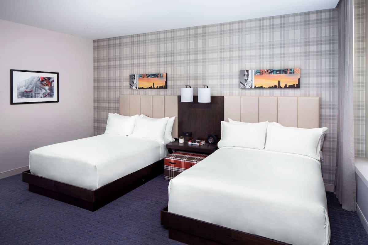 A hotel room with two beds, a plaid-patterned wall, and artwork above the beds.