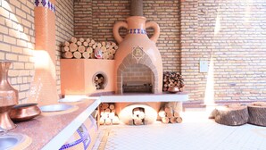 A brick oven with a decorative design, a tiled backsplash, and a rustic wooden table with a metal bowl. - Rakat Plaza (Tashkent)