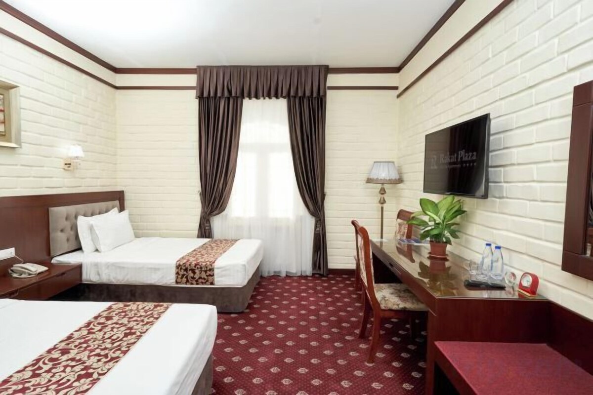 Habitación de hotel con dos camas, un escritorio, una silla, un televisor y una ventana con cortinas.
