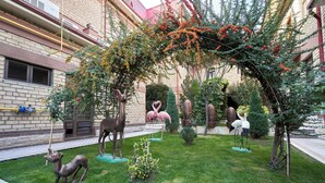 A courtyard with a brick building, a small lawn, and various sculptures including a deer, flamingos, and a heart-shaped structure. - Rakat Plaza (Tashkent)