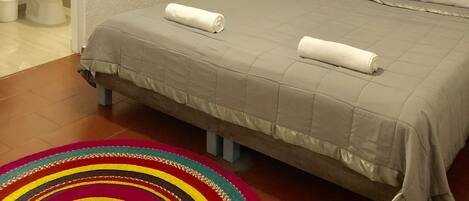 A bedroom with a bed, a ceiling fan, a nightstand, a wall-mounted dreamcatcher, and a colorful rug.