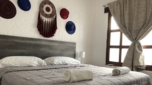 Un lit bien fait, avec une couverture grise, des oreillers blancs et une serviette blanche roulée posée sur le lit.