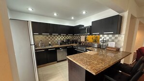 Une cuisine moderne avec des meubles de couleur sombre, des comptoirs en granit, des appareils électroménagers en acier inoxydable et un îlot central doté de tabourets de bar.