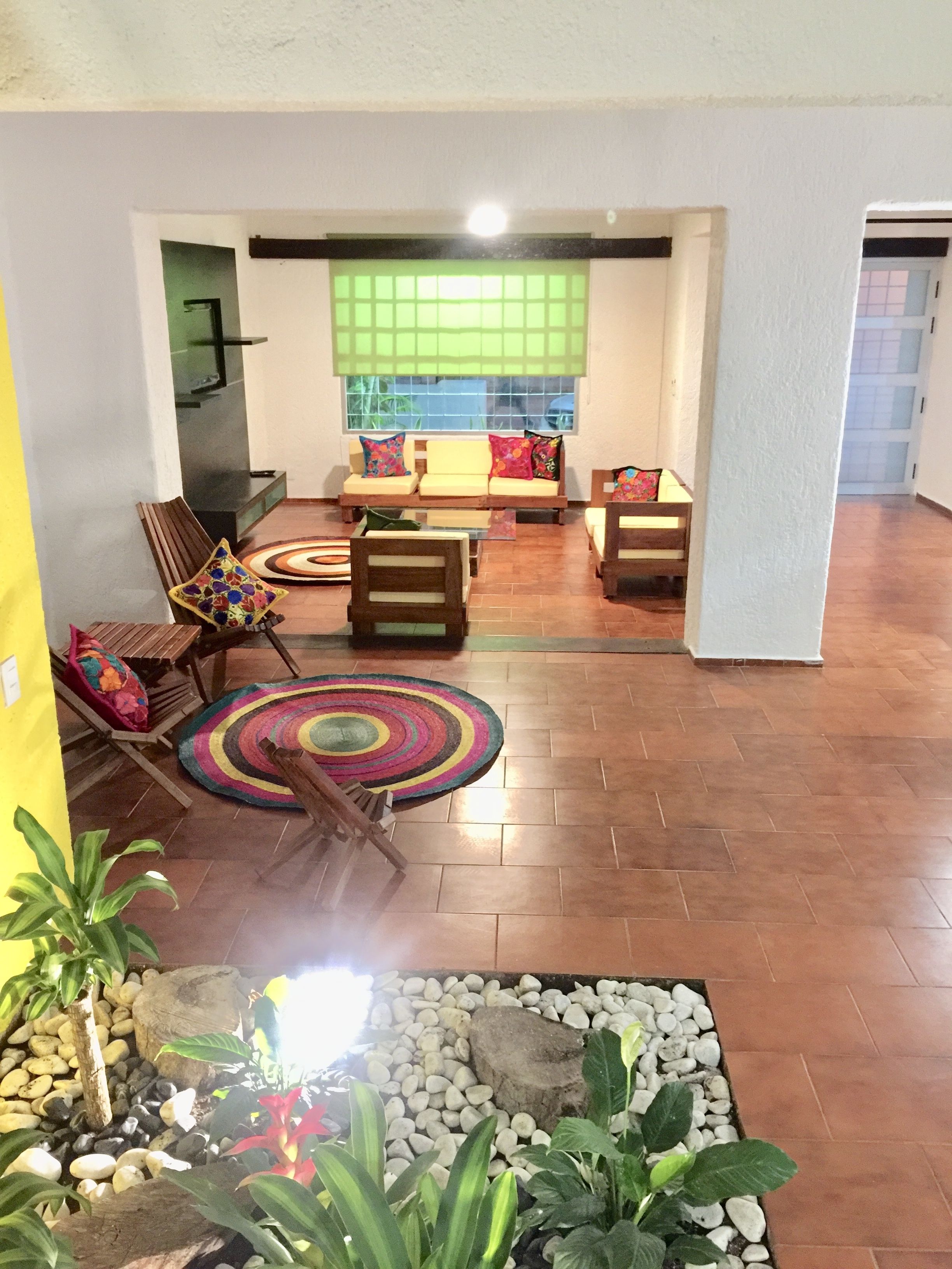 A living room with a sofa set, a coffee table, and a patterned rug. There is a small garden area with plants and rocks.