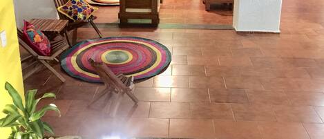 A living room with a sofa set, a coffee table, and a patterned rug. There is a small garden area with plants and rocks.