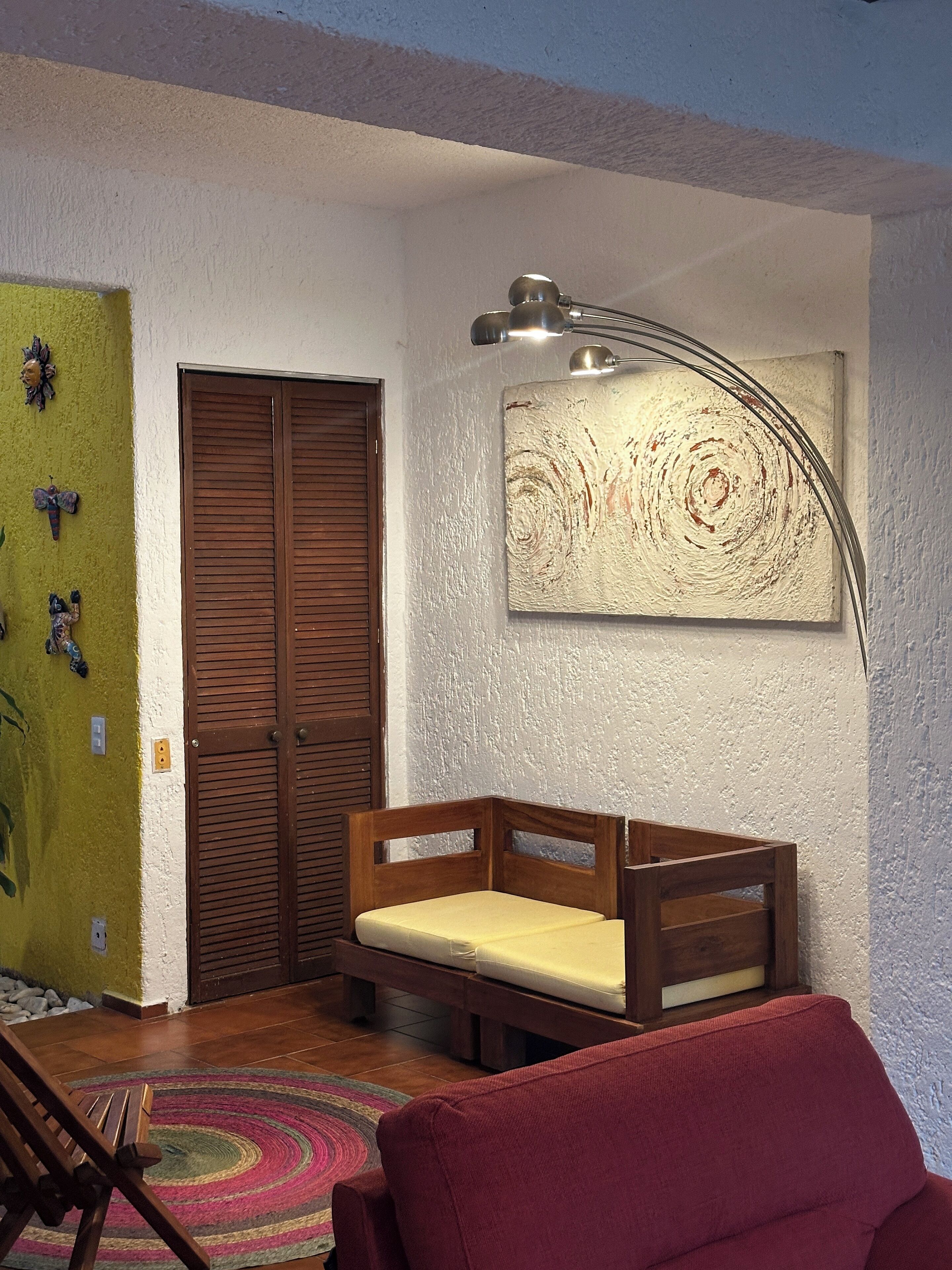 A room with a wooden bench, a red chair, a wall-mounted lamp, and a door with wooden shutters.