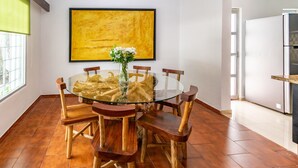 Un coin repas avec une table ronde en verre entourée de chaises en bois, un vase rempli de fleurs et un grand tableau jaune accroché au mur.