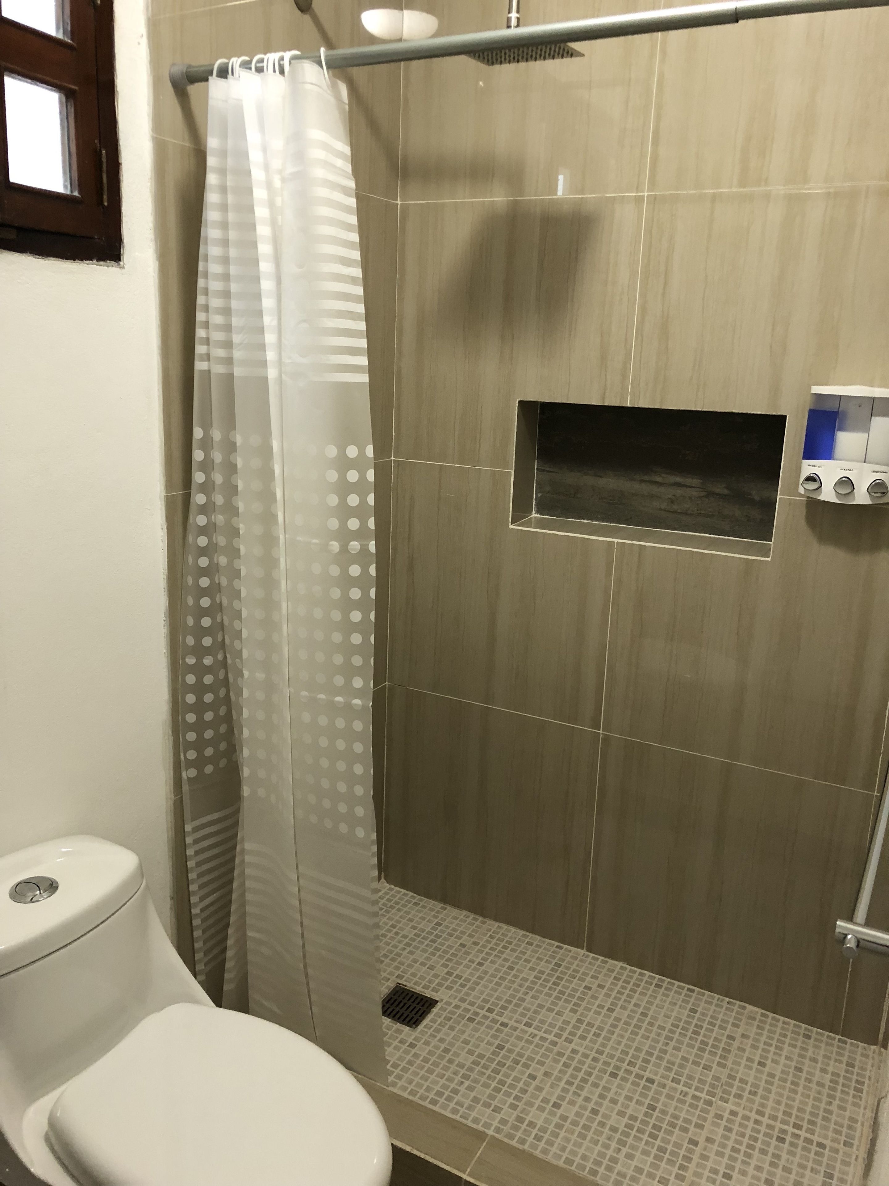 A bathroom with a toilet, shower, and a control panel for water temperature and flow.