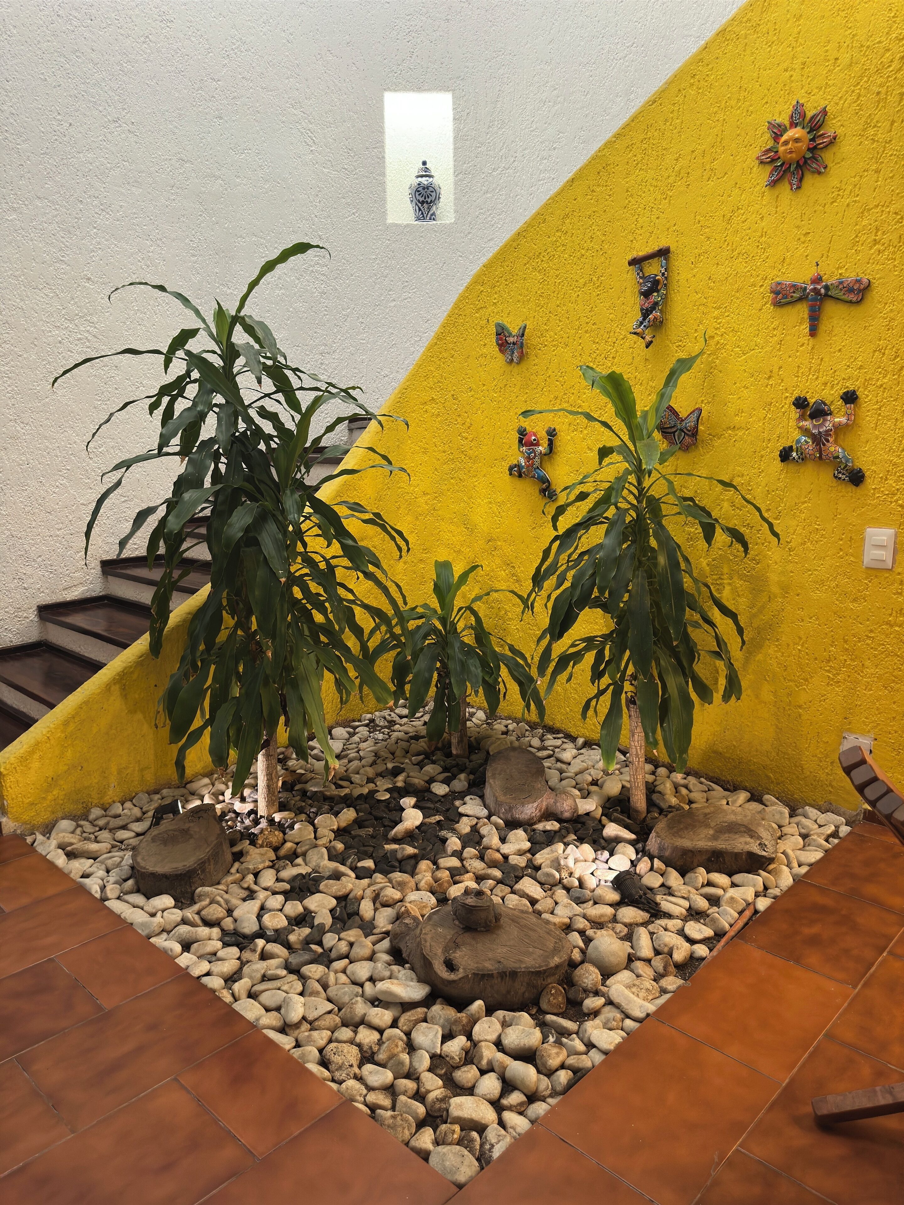 A small indoor garden with potted plants, decorative wall art, and a tiled floor.