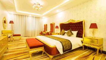 A luxurious hotel room with a large bed, ornate headboard, and a striped carpet.