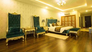 A spacious bedroom with a large bed, two ornate chairs, a nightstand, and a decorative wall panel. - Anh Nguyet Hotel (An Xuyen)