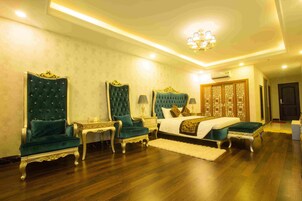 Um quarto espaçoso com uma cama grande, duas cadeiras elaboradas, uma mesinha de cabeceira e um painel decorativo na parede.