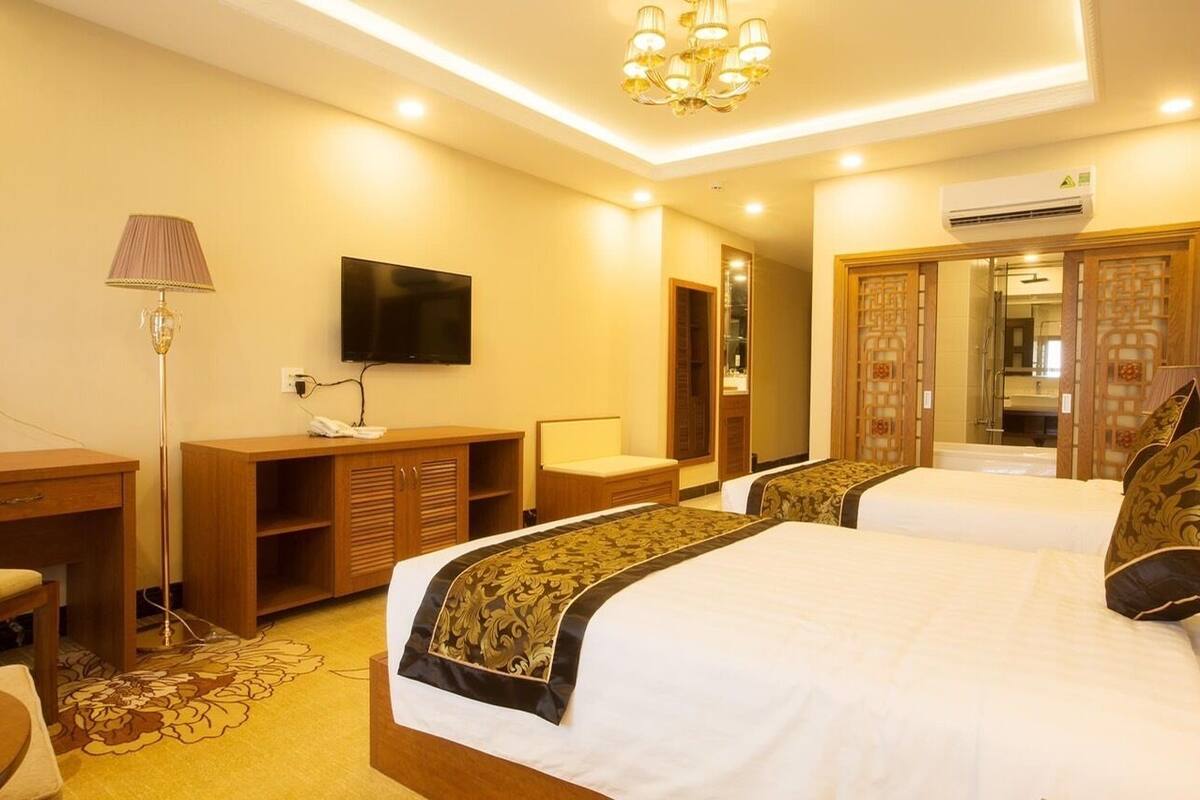 A hotel room with two beds, a TV, a desk, a lamp, and a wardrobe.