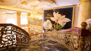 An ornate staircase with a marble floor and golden railings, leading to a room with a large floral painting and a chandelier. - Anh Nguyet Hotel (An Xuyen)