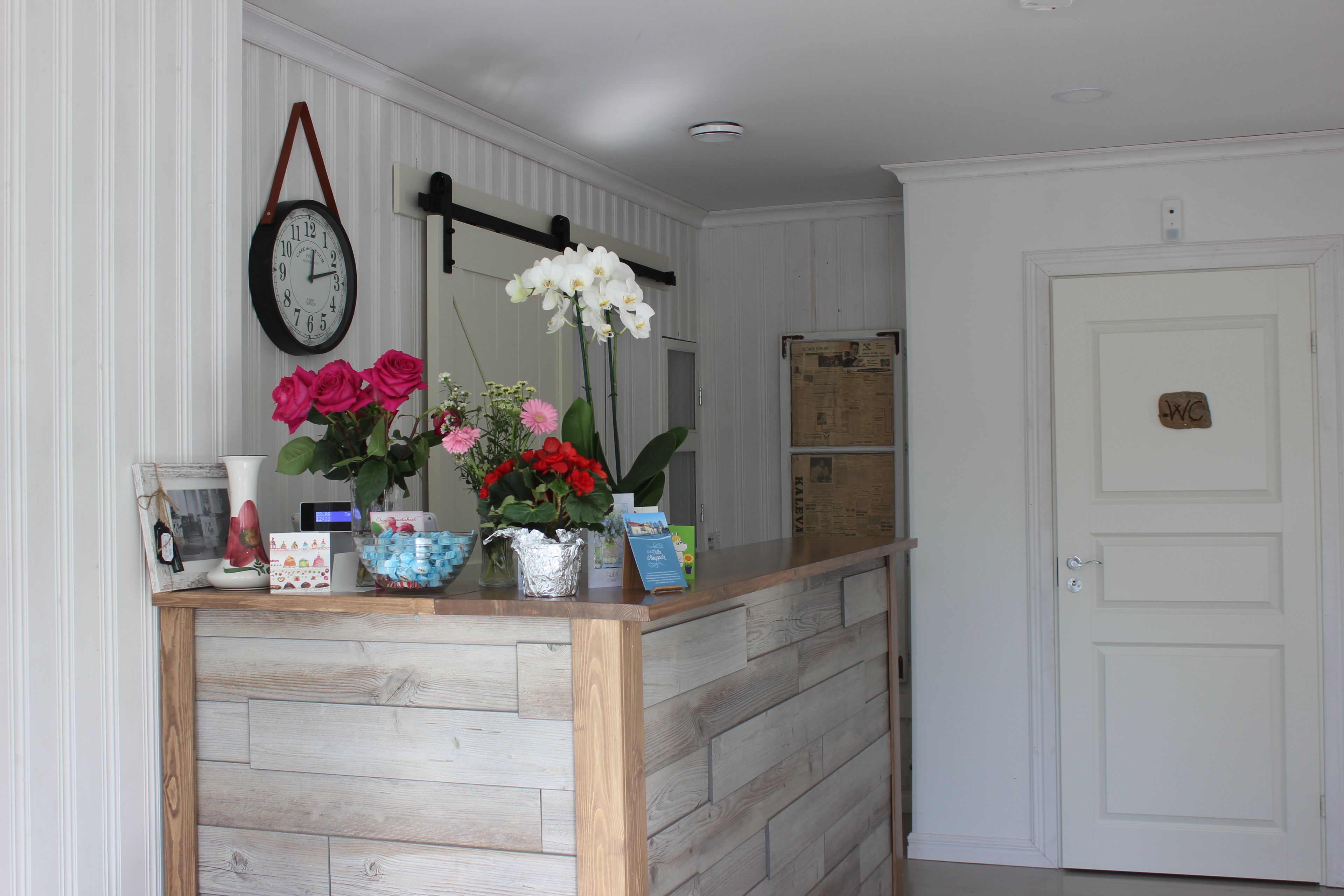 A reception desk with a clock, flowers, and a door labeled "WC".