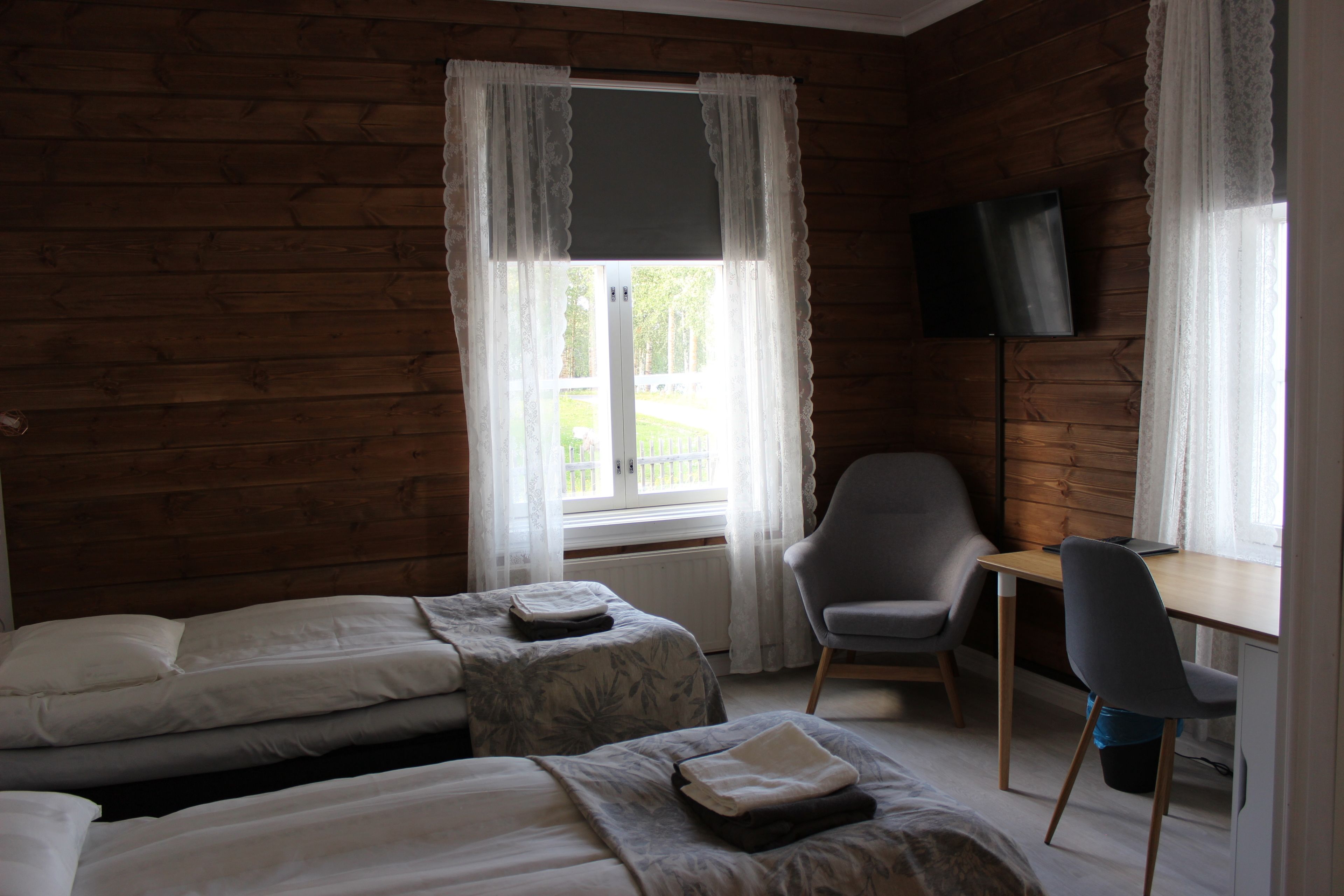 Una habitación con paredes de madera, dos camas, un escritorio, una silla y un televisor.
