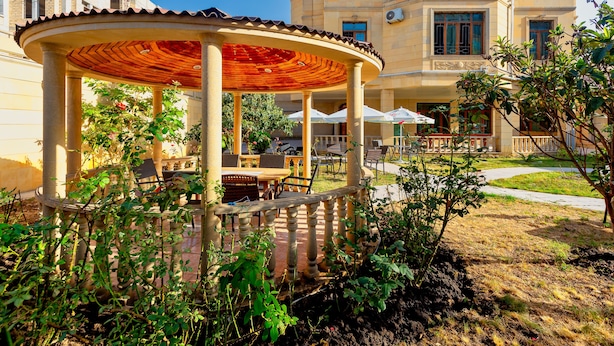 A covered outdoor seating area with tables and chairs, surrounded by greenery and a building in the background. - STAR Hotel (Baku)