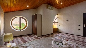 A hotel room with a wooden ceiling, a round window, a bed with a patterned bedspread, and a bedside table with a lamp. - STAR Hotel (Baku)