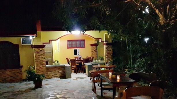 An outdoor patio area with stone flooring, wooden tables and chairs, and potted plants.