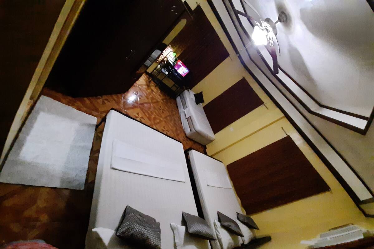 A room with two white beds, a ceiling fan, and a television in the background.