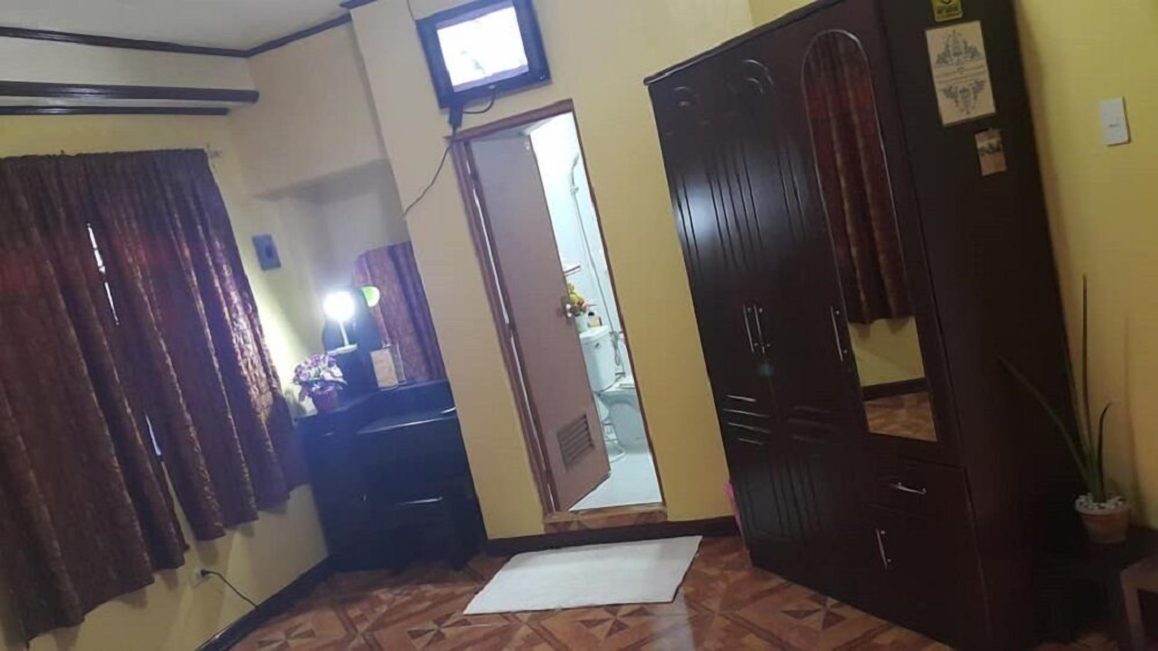 Una habitación con un armario de madera, un espejo, una mesita con lámpara y una planta en maceta.