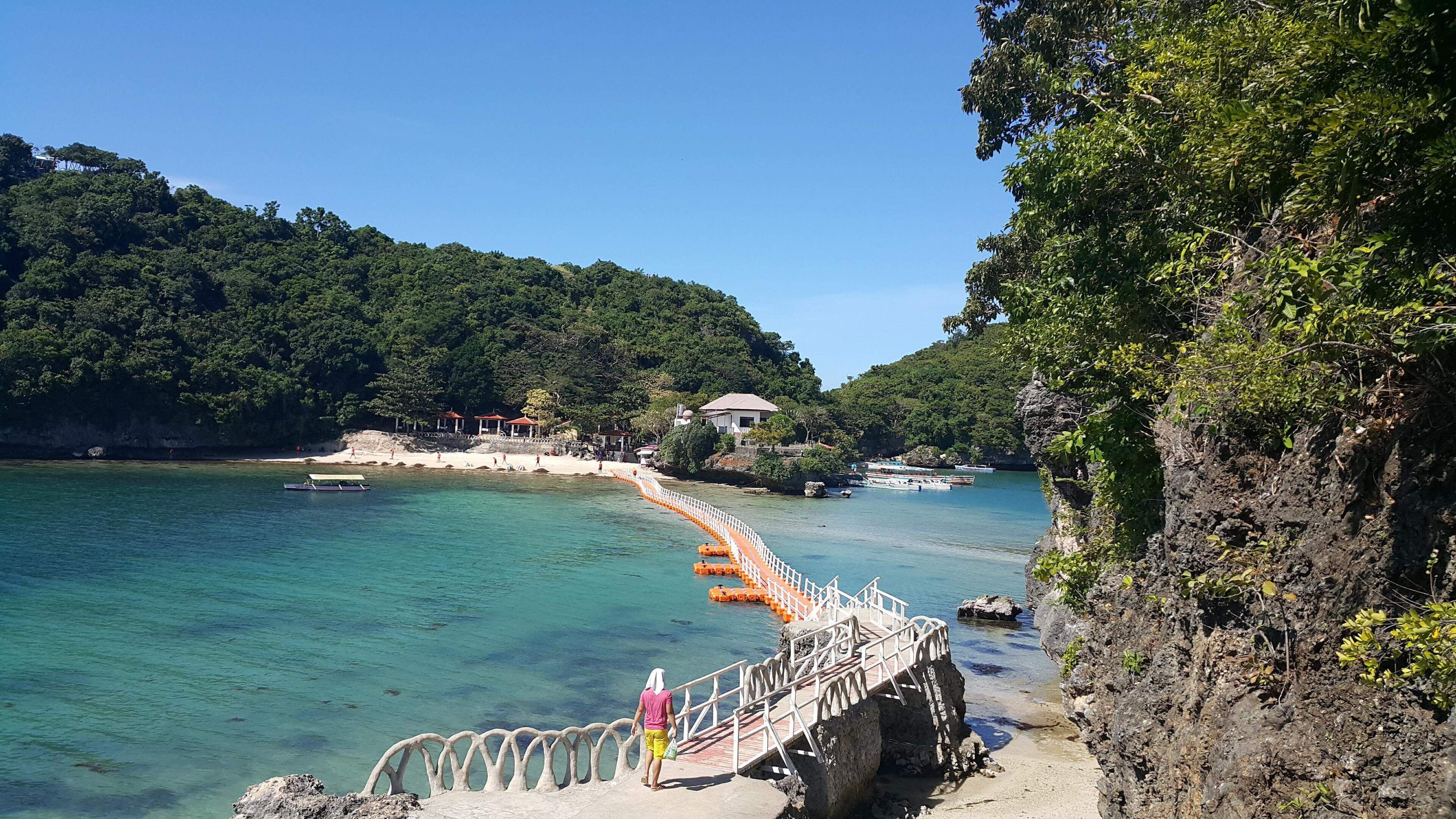 Una zona costera con un camino de madera que lleva a una playa, rodeada de exuberante vegetación y aguas azules cristalinas.