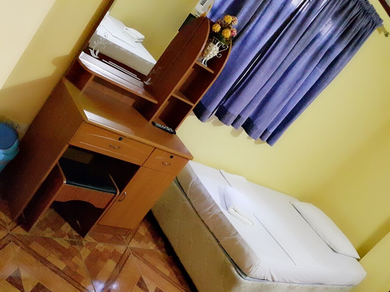 A room with a wooden desk, a bed, and a window with blue curtains.