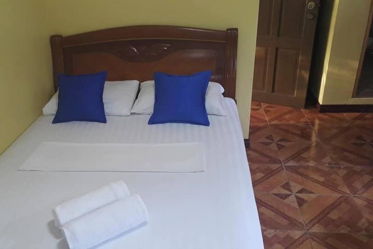 A bed with white bedding, two blue pillows, and a folded white towel.