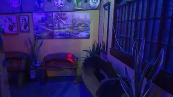 Een kamer met weinig licht, met een bank, een tafel en een raam met jaloezieën.