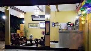 A reception area with a tiled floor, wooden furniture, a counter with a plant, and framed artwork on the wall.