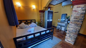 A hotel room with a bed, a wardrobe, a bathroom, and a stone pillar.