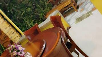 An outdoor dining area with a table and chairs, surrounded by greenery and a yellow wall.