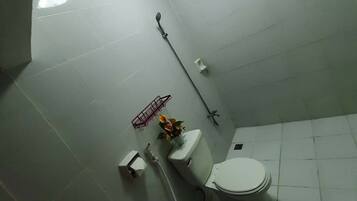 A small, tiled bathroom with a toilet, bidet, and a small shelf with a flower vase.