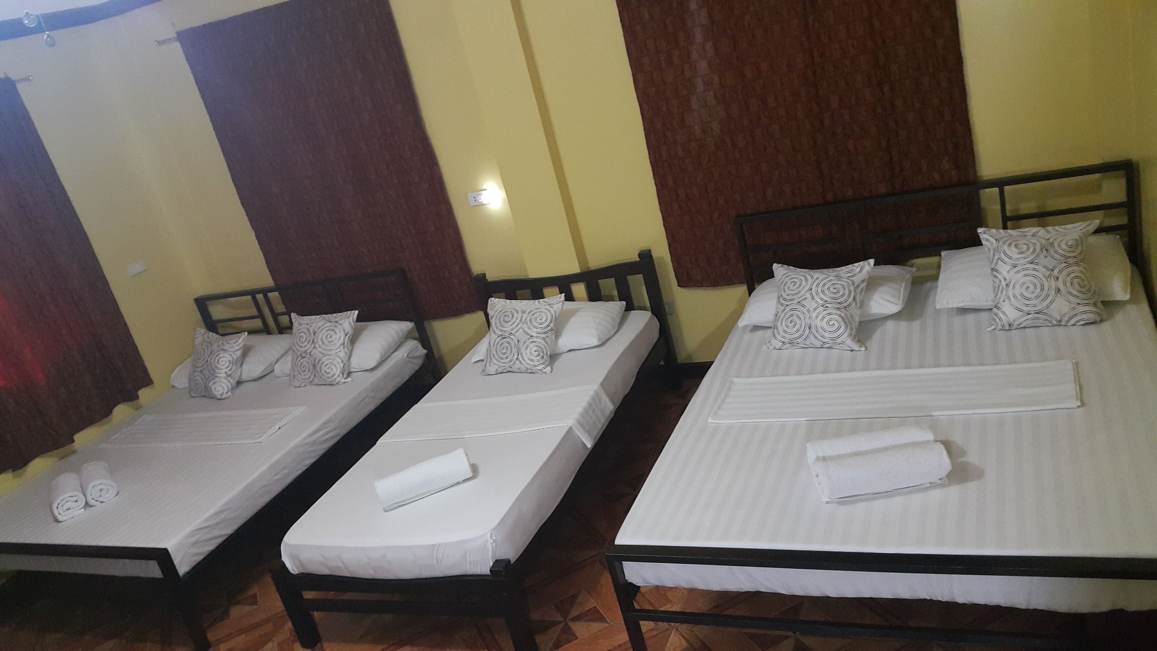 Three single beds with white linens and patterned pillows, wooden headboards, and a tiled floor.