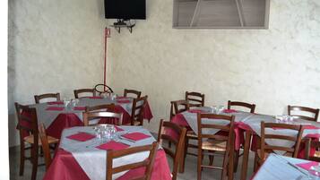 A restaurant with multiple tables covered with red and white tablecloths, wooden chairs, and a television mounted on the wall.