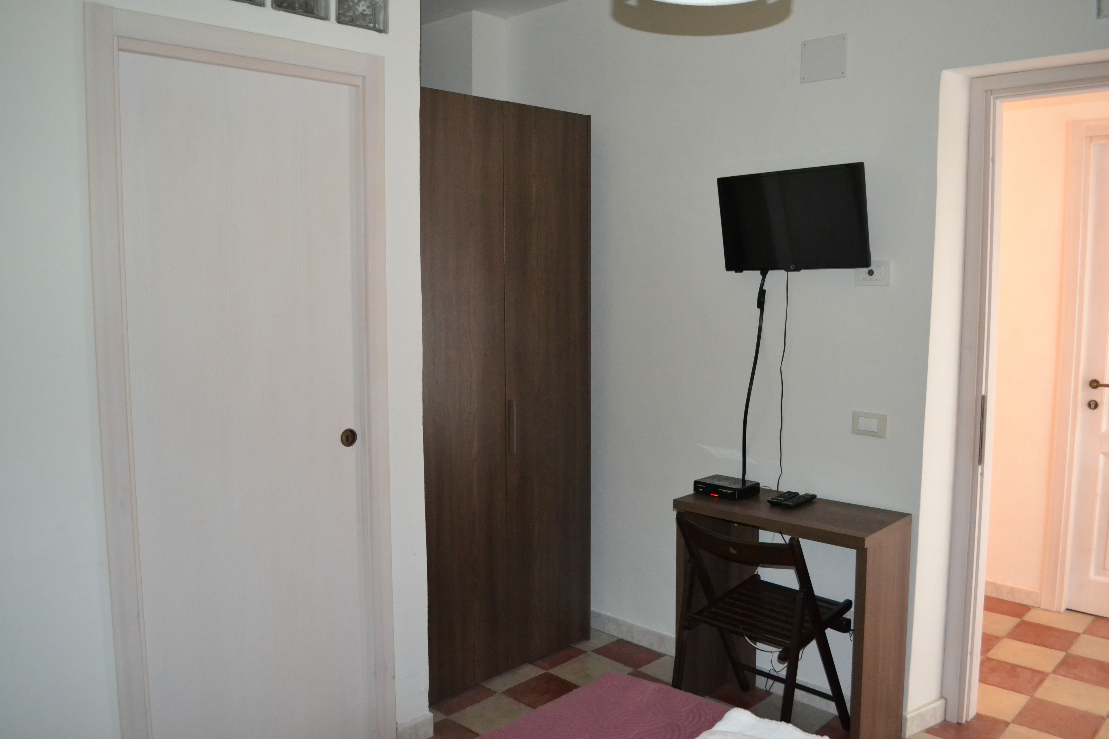 A room with a bed, a desk with a chair, a television mounted on the wall, and a wardrobe.