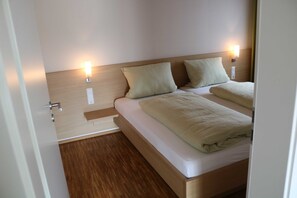 Une chambre d’hôtel avec une tête de lit en bois, deux lits et des lampes de chevet.