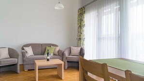 Ein Wohnzimmer mit zwei grauen Sofas, einem Holztisch und einem Esstisch mit einem grünen Tischläufer.