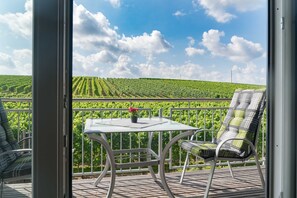 Un balcon avec une table et des chaises, donnant sur un vignoble.