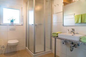 A bathroom with a toilet, a shower with a glass door, a sink with a marble countertop, and a window with a plant.