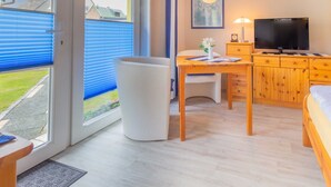 Una habitación con cama, escritorio, silla, televisor y ventana con persianas.