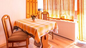 A dining area with a table set for two, wooden chairs, a vase with flowers, and a window with curtains. - Holiday apartment - FH VIL 0062 (Patzig)