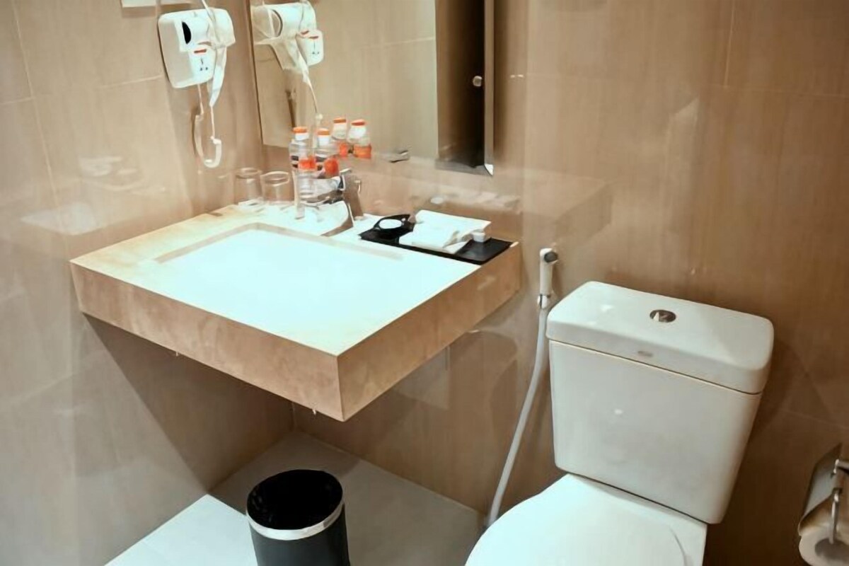 Une salle de bain équipée d’un lavabo, d’un miroir, de toilettes et d’une poubelle.