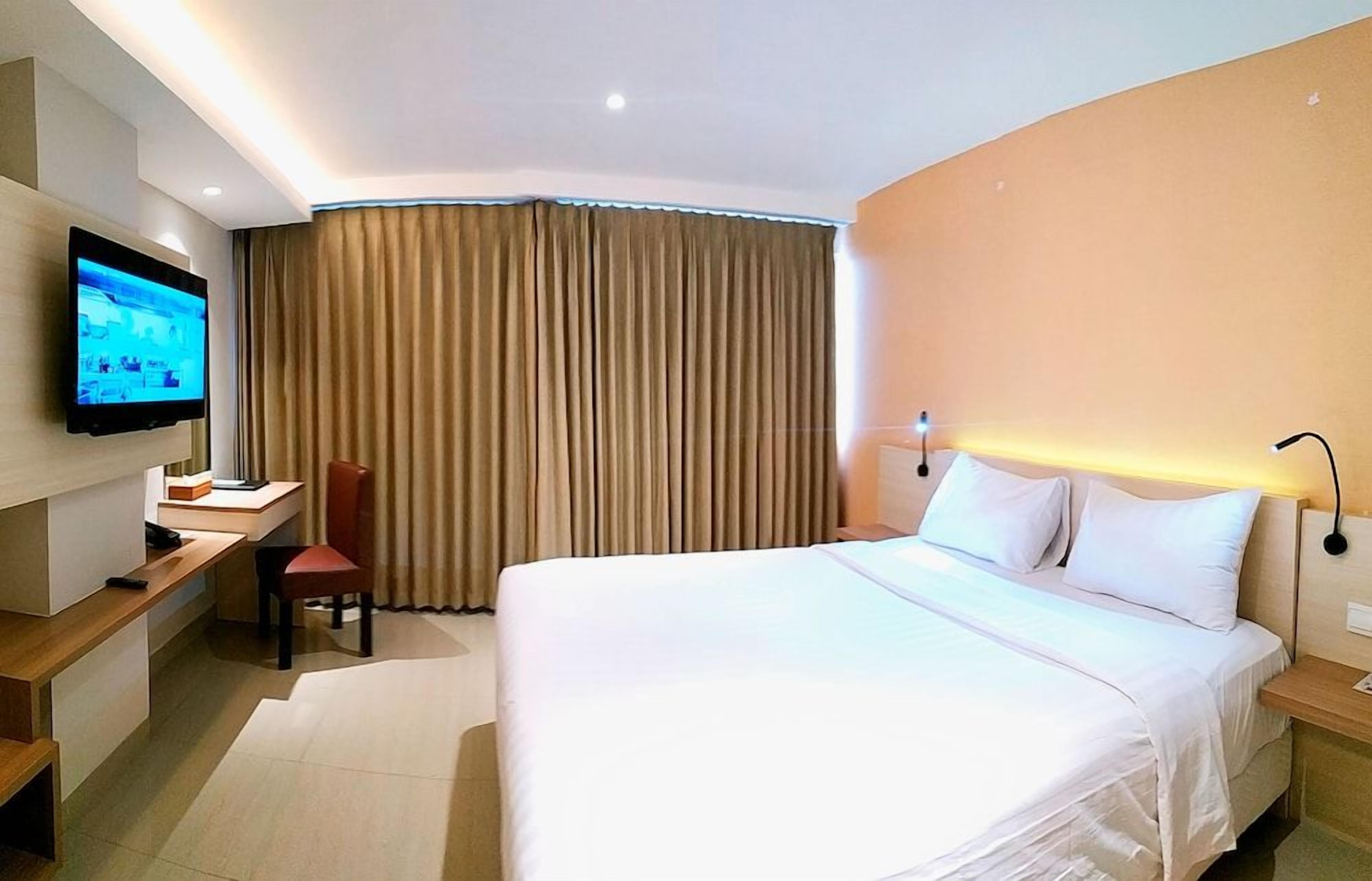 Une chambre d’hôtel avec un grand lit, un bureau, une chaise, une télévision et une fenêtre avec des rideaux.