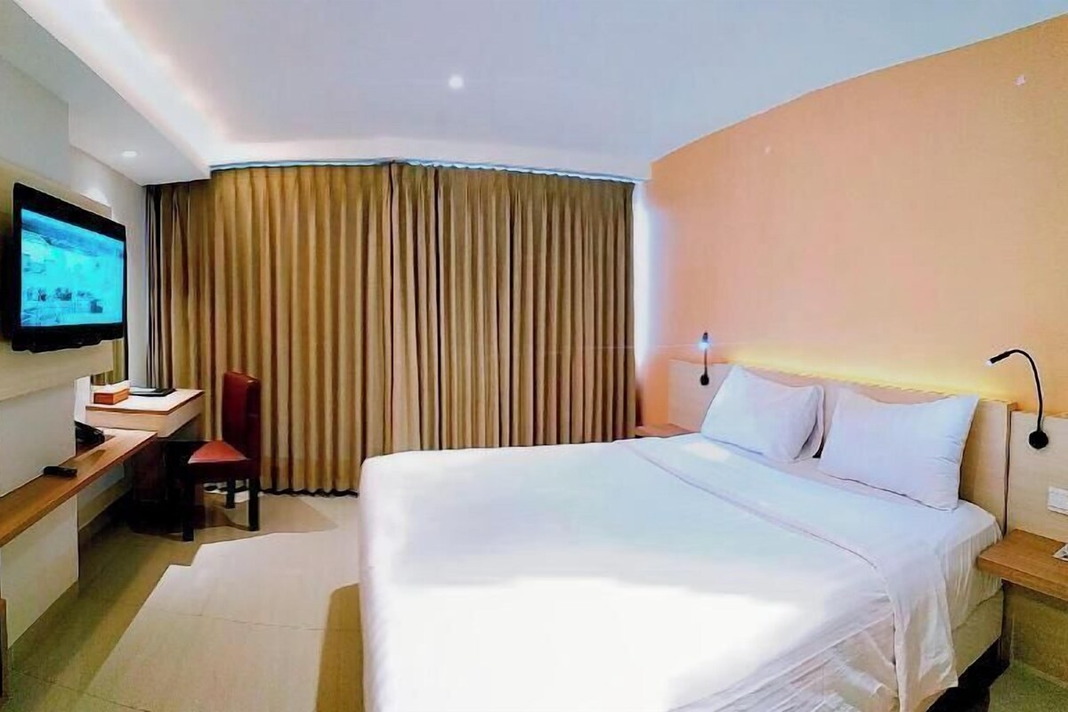 Une chambre d’hôtel avec un lit, un bureau, une chaise, une télévision et un rideau.