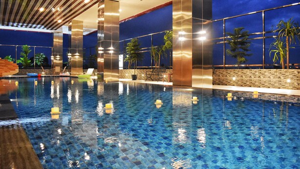 Une piscine intérieure à l’eau d’un bleu cristallin, entourée de murs offrant une vue sur des palmiers et le ciel nocturne.