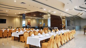 Une salle de conférence avec de longues tables disposées pour un événement formel, équipée de chaises et de couverts.