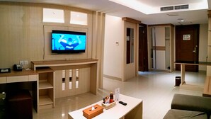 Un salon moderne avec un téléviseur à écran plat fixé à un mur en bois, un petit bureau avec un téléphone et un coin salon confortable avec des coussins.